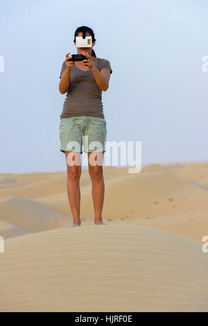 Donna (in 40s) indossando una realtà virtuale auricolare (VR) di maschera e giocare nel deserto. Foto Stock