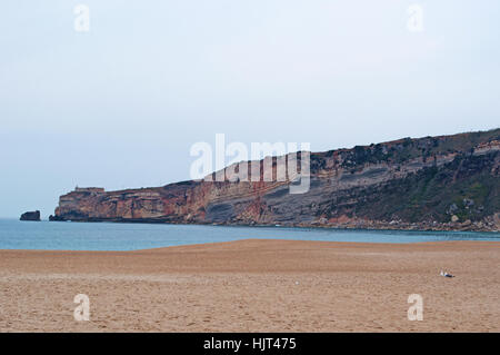 Portogallo: vista della spiaggia, del sitio, il vecchio quartiere della città di Nazare arroccato su una rupe e il faro Foto Stock