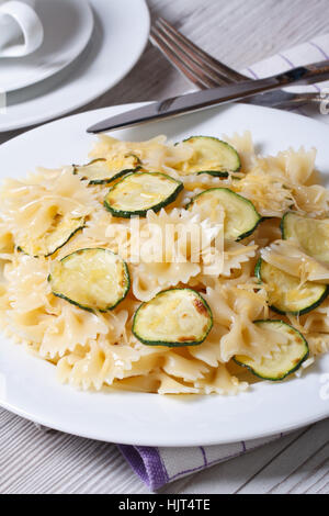 Farfalle di pasta con le fette di zucchine closeup su una piastra bianca con coltello e forchetta sulla verticale della tabella Foto Stock