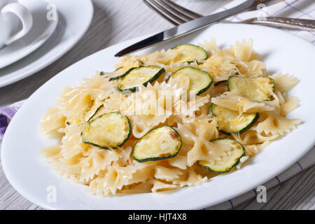 Farfalle di pasta con le fette di zucchine closeup su una piastra bianca con una forcella sul tavolo orizzontale Foto Stock