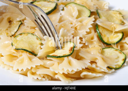 Farfalle di pasta con fette di zucchine, il formaggio e una forcella su una piastra bianca orizzontale macro Foto Stock