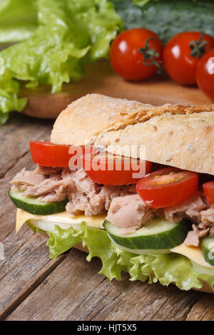 Delizioso sandwich con tonno e verdure closeup sullo sfondo degli ingredienti sulla vecchia scrivania verticale. Foto Stock