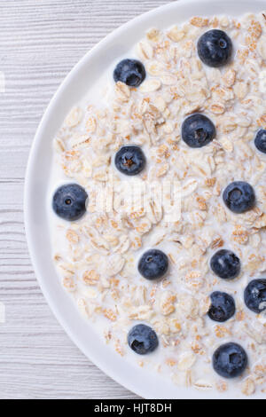 Farina di avena con latte e mirtilli closeup su sfondo di legno. vista dall'alto in verticale Foto Stock