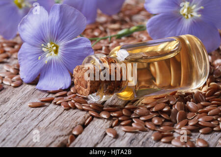 Semi di lino, fiori blu e olio in una bottiglia sul tavolo di close-up orizzontale Foto Stock