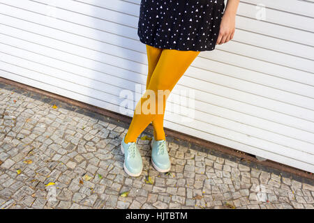 Gambe femmina giallo da indossare collant e scarpe verdi contro il muro bianco e pietre portoghesi marciapiede Foto Stock