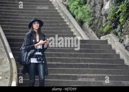 Turista (donna) camminando giù per le scale a Budapest, vestita in pelle nera, con foto e fotocamera hat Foto Stock