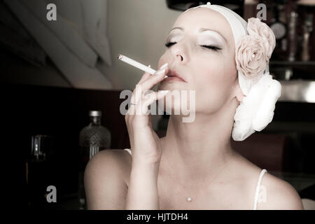 Ritratto di una donna con sigaretta e acconciatura retrò. Foto di moda. Fiori in testa. Somiglia all'infiorescenza. Donna che fuma Foto Stock