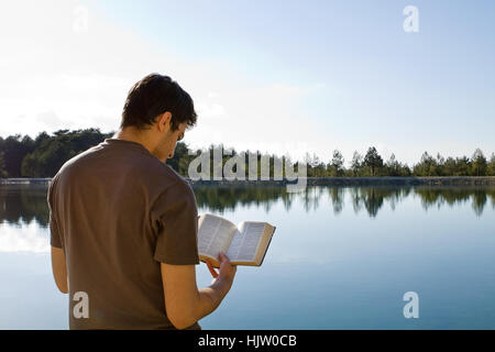 Giovane uomo di fronte al lago di lettura della Bibbia (King James Version) Foto Stock