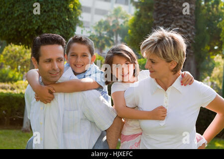 Due genitori dando piggyback giostre per due bambini Foto Stock