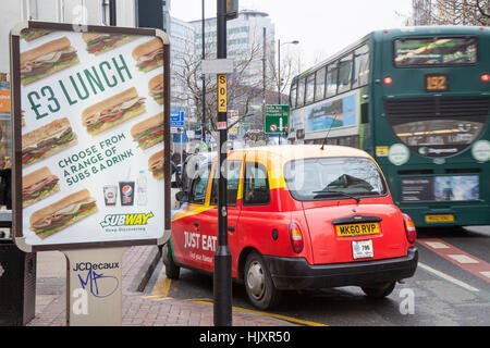 £3 pranzo Bill bordo & Just Eat pubblicità sul taxi rosso giallo Manchester; veicolo pubblicità con Subway offerta speciale su bannerstand, Centro Città, Regno Unito Foto Stock