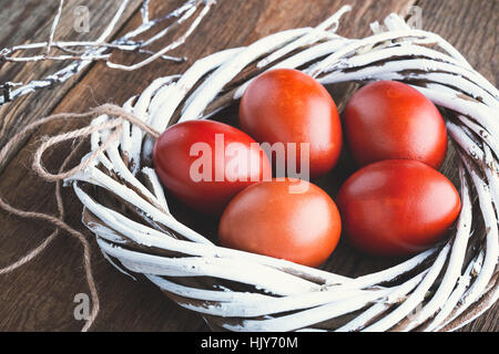 Pasqua dipinte di rosso le uova in salice bianco corona sul rustico in legno tabella Foto Stock