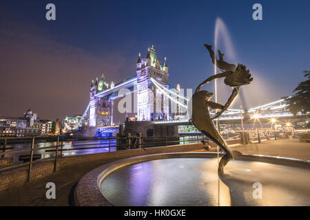 La ragazza con una fontana dei Delfini telai Tower Bridge si riflette nel fiume il Tamigi di notte, Londra, Inghilterra, Regno Unito Foto Stock