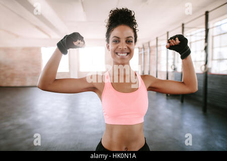 Ritratto di giovane donna fitness la flessione di muscoli e sorridente. African modello femminile in abbigliamento sportivo che mostra i suoi muscoli. Foto Stock