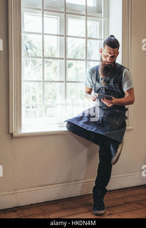 Parrucchiere con tavoletta digitale seduto sul davanzale di salon. Barba uomo con tavoletta digitale al barbiere. Foto Stock