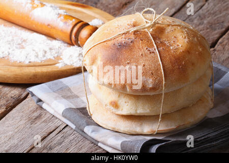 Pane appena sfornato pane pita su una tavola di legno di close-up. mattarello e farina in background. orizzontale Foto Stock