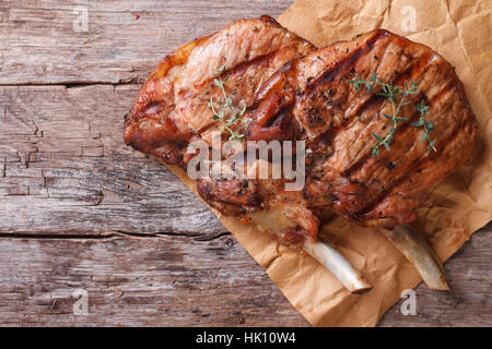 Due pezzi di carne di maiale alla griglia su carta su un vecchio tavolo orizzontale vista da vicino Foto Stock