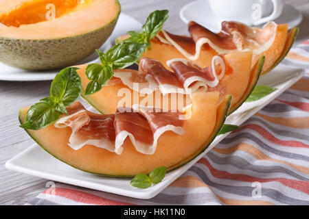 Il Melone con prosciutto e basilico close-up su una piastra bianca orizzontale. Foto Stock