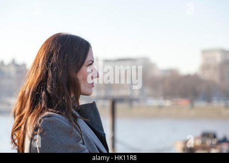 Una donna attraente con lunghi capelli scuri si affaccia su un fiume Foto Stock