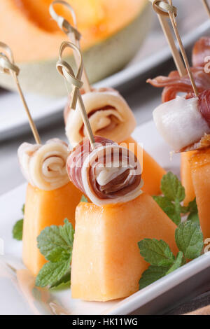 Finger food: prosciutto di Parma e melone su spiedini su una piastra macro verticale. Foto Stock