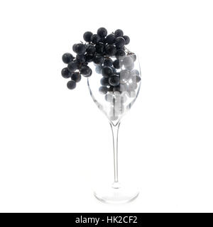Concetto di trasformazione alimentare e di vinificazione. Grappolo di uva nera nel vino rosso vetro appesi sopra isolata contro il bianco puro sfondo. Foto Stock