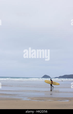 Un lone surfer braves il freddo e di imprese in una linea di vuoto a Cornish Beach, Perranporth. Foto Stock