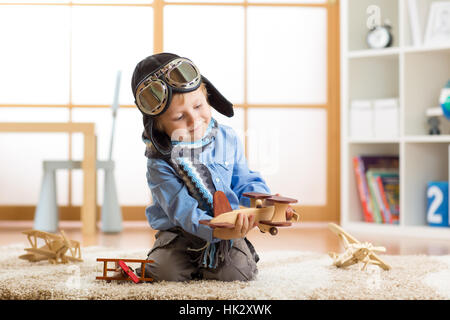 Capretto piccolo ragazzo sogni essere un aviatore e gioca con gli aeroplani giocattolo seduto sul pavimento nella nursery room Foto Stock