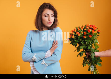 Arrabbiato offeso giovane donna in piedi con le braccia incrociate e la ricezione di bouquet di fiori su sfondo giallo Foto Stock