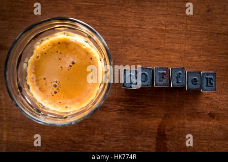 Caffè Espresso con crema nel rotondo in vetro su di un legno compensato di sfondo con gomma timbro di inchiostro scritte al lato ancora vita piatta fotografia laici Foto Stock