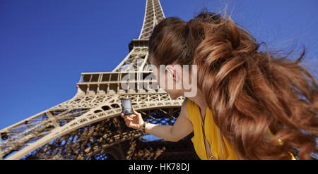 Turistica, senza dubbio, ma ancora in modo divertente. Visto da dietro il giovane donna prendendo foto con una fotocamera digitale contro la Torre Eiffel a Parigi, Francia Foto Stock