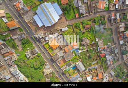 Una fotografia aerea aerea cattura un fitto quartiere residenziale con un mix di case unifamiliari, piccoli edifici e strutture più grandi con tetti blu e arancioni. Corre una strada principale Foto Stock