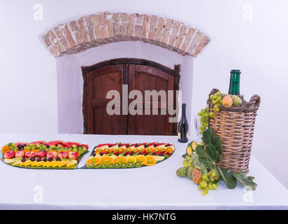 Composizione di frutta e tagliare il vetro rivestito demijohn per vino vimini. Su un tavolo pieno di un ristorante, con uva, fichi, fichidindia e foglie. Un Foto Stock