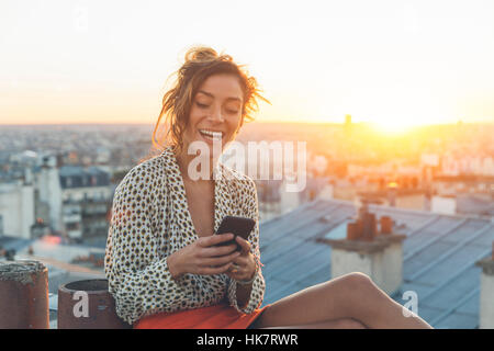 Donna che utilizza un telefono intelligente sui tetti di Parigi Foto Stock