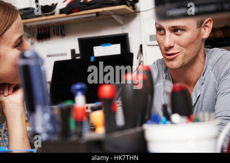 Una giovane donna e uomo taling reciprocamente in una tecnologia di laboratorio o di officina di riparazione, con strumenti sul tavolo. Foto Stock