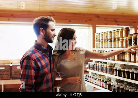 Un giovane uomo e donna scegliendo da un display di conserve di produrre in una farm shop. Foto Stock