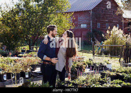 Un giovane uomo e donna abbracciando tra mostra di piante in un giardino centrale. Foto Stock