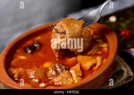 Primo piano di un vaso di terracotta con lo spagnolo callos, una tipica carne di manzo stufato di trippa con i ceci, morcilla e chorizo, su una tavola in legno rustico Foto Stock