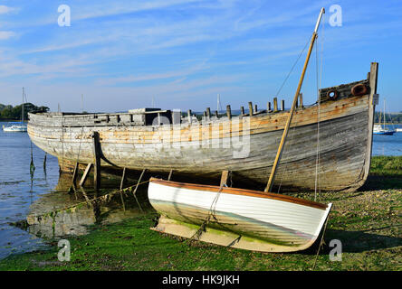 Vecchio scafo in bisogno di riparazione per la vendita accanto a un gommone a bassa marea a Dell Quay a Chichester Harbour, West Sussex, Inghilterra, Regno Unito Foto Stock