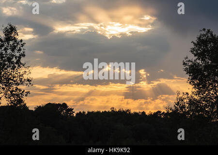 I raggi di luce del sole da dietro le nuvole al tramonto Foto Stock