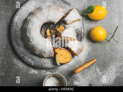 In casa senza glutine bundt di limone la torta con lo zucchero in polvere servito con appena raccolto limoni su cemento grigio Sfondo, vista dall'alto Foto Stock