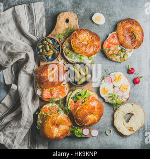 Varietà di bagel con salmone affumicato, uova, Rafano, avocado, cetriolo, verdi e crema di formaggio per colazione, pranzo sano, parte o da asporto su legno Foto Stock