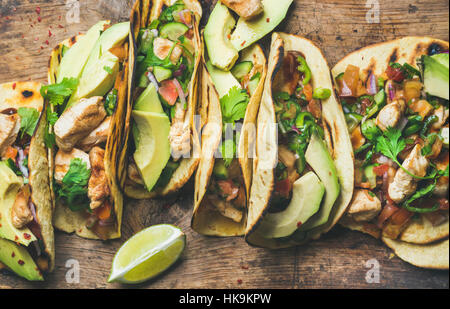 Tacos con pollo alla griglia, avocado, salsa fresca e salsa di limes su legno rustico sfondo, vista dall'alto. Una sana il carburatore basso e basso tenore di grassi il pranzo o cibo f Foto Stock