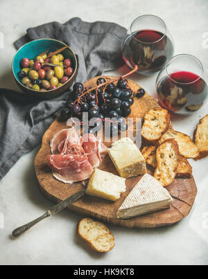 Vino e snack set. Varietà di formaggio, olive, prosciutto arrosto baguette fette, uva sulla tavola di legno e bicchieri di vino rosso su marmo grigio ba Foto Stock