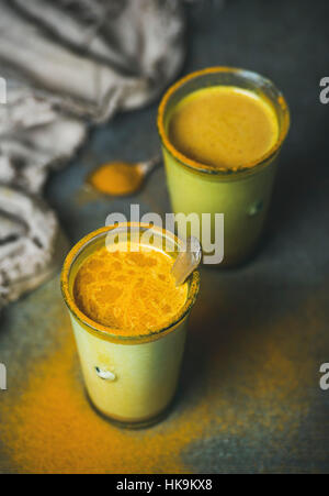 Golden latte con la curcuma in polvere in bicchieri su sfondo scuro. Per la salute e l'energia aumentando, influenza rimedio naturale a freddo drink di combattimento. Pulire mangiare, d Foto Stock