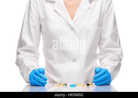 Pila di diverse compresse e capsule su tavola nella parte anteriore del medico donna in bianco camice blu e sterilizzare guanti chirurgici contro white Foto Stock