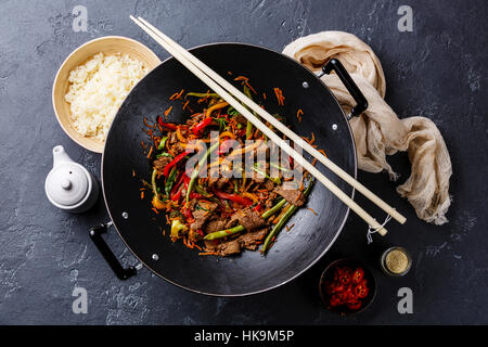 Rosolare la carne di manzo con verdure e riso in un wok padella in pietra scura sullo sfondo Foto Stock