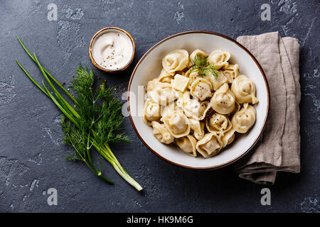 Pelmeni russo gnocchi di carne con salsa di panna acida e verdi nel recipiente in pietra scura sullo sfondo Foto Stock