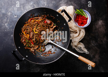 Soffriggere per la sua pasta di soba con manzo e verdure in padella wok su sfondo scuro Foto Stock