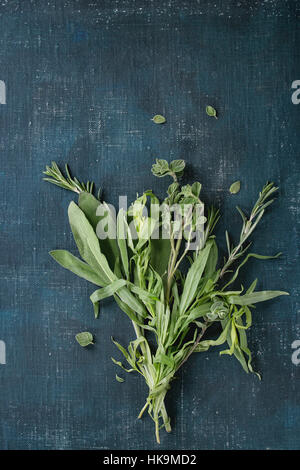 Bundle di fresche erbe italiano rosmarino, origano e salvia su blu scuro dello sfondo squallido. Vista da sopra con lo spazio di copia Foto Stock