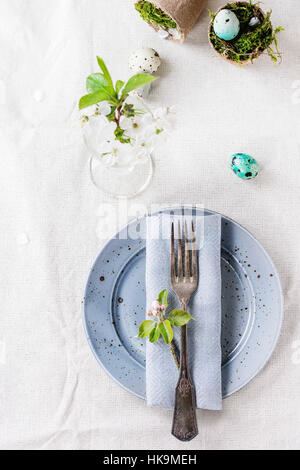 Impostazione tabella decor colorato Pasqua uova di quaglia con molla di fiori di ciliegio, moss in vasi da giardino, le placche vuote, vintage posate sulla tovaglia bianca. T Foto Stock