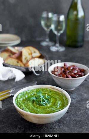 La rucola erba cipollina pesto di basilico servito in una ciotola di ceramica con crostini, mandorle e vino. Fotografato fron vista frontale su un nero/sfondo marrone. Foto Stock
